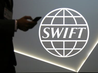 A man using a mobile phone passes the logo of global secure financial messaging services cooperative SWIFT. Reuters