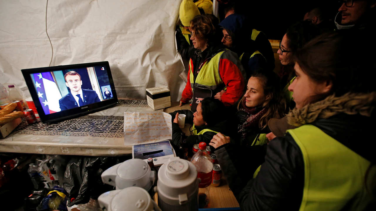 Protesters wearing yellow vests watch French President Emmanuel Macron on a TV screen at the motorway toll booth in La Ciotat, near Marseille, France, December 10, 2018. REUTERS/Jean-Paul Pelissier - RC15BFDC7570
