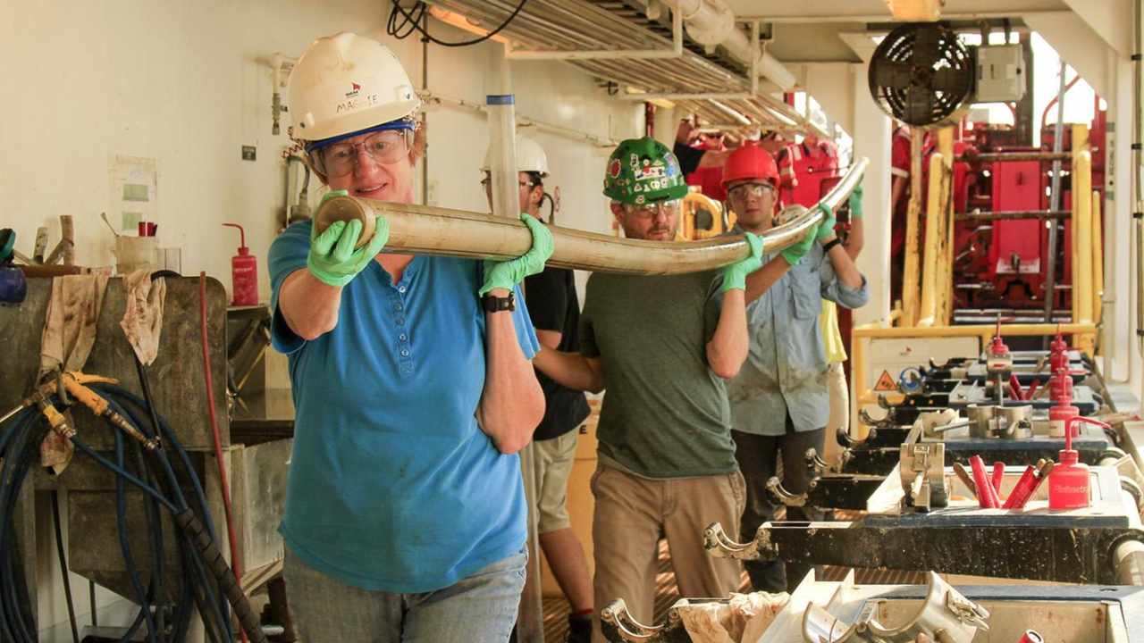 Scientists carry a core of rock extracted by drill. Image credit: Carlos Alvarez-Zarikian/Chicago News