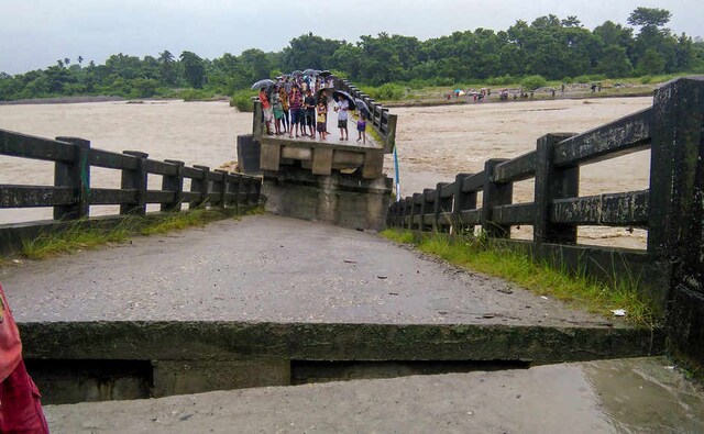 Villagers look on at a bridge which collapsed following incessant rainfall in their inundated village near Sujanghat, in Baksa district of Assam. PTI Villagers look on at a bridge which collapsed following incessant rainfall in their inundated village near Sujanghat, in Baksa district of Assam. PTI