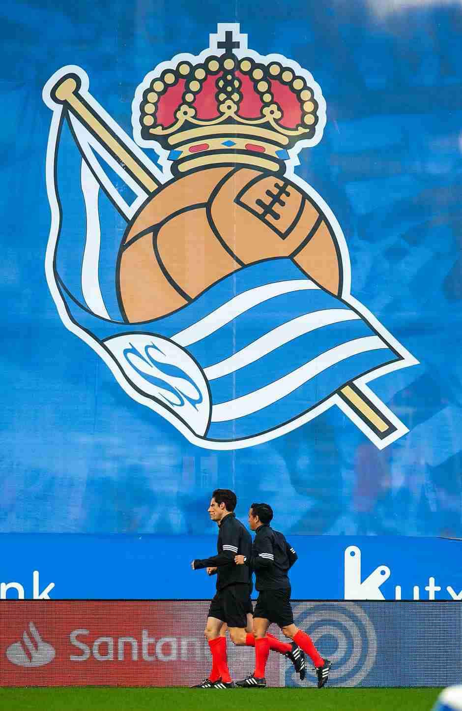 Real Sociedad’s blue and white colours pay homage to the cities official flag: a blue canton on a white field which also gave credence to their nickname ‘Txuriurdin’ meaning blue and white. Like Real Madrid, the crown, which adorns a football, was added after King Alfonso XIII gave the club his patronage thus making Sociedad ‘Real’. Real Sociedad’s blue and white colours pay homage to the cities official flag: a blue canton on a white field which also gave credence to their nickname ‘Txuriurdin’ meaning blue and white. Like Real Madrid, the crown, which adorns a football, was added after King Alfonso XIII gave the club his patronage thus making Sociedad ‘Real’.