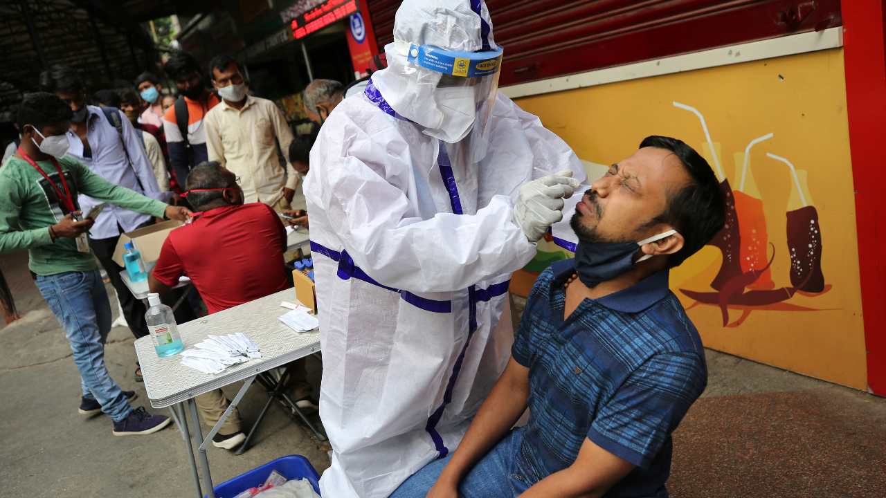 A health worker in protective suit collects nasal swab of a traveler to test for COVID-19 outside a train station in Bengaluru, India, Sunday, April 11, 2021. India is reporting a surge in infections, which according to experts is due in part to growing disregard for social distancing and mask-wearing in public spaces. (AP Photo/Aijaz Rahi)