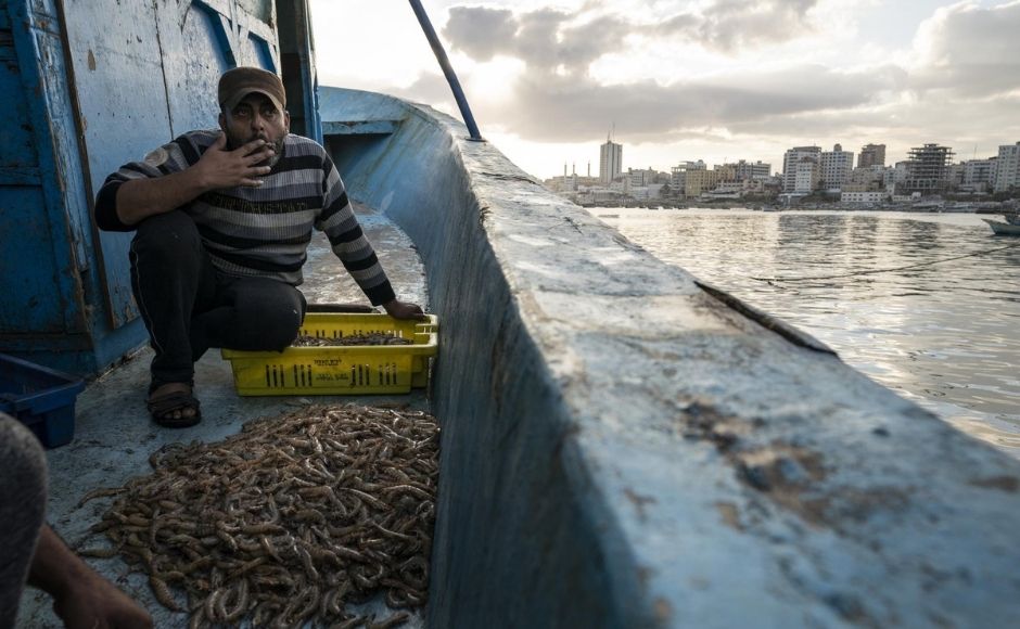 The recent war saw Israel unleash hundreds of airstrikes across Gaza at what it said were Hamas militant targets. Hamas and other armed groups fired more than 4,000 rockets toward Israel, most of which were intercepted or landed in open areas. At least 243 Palestinians were killed, as were 12 people in Israel. | In the picture: A fisherman takes a drag from his cigarette while sorting shrimp on deck in Gaza City on Sunday, 23 May, 2021. Photo via The Associated Press/John Minchillo