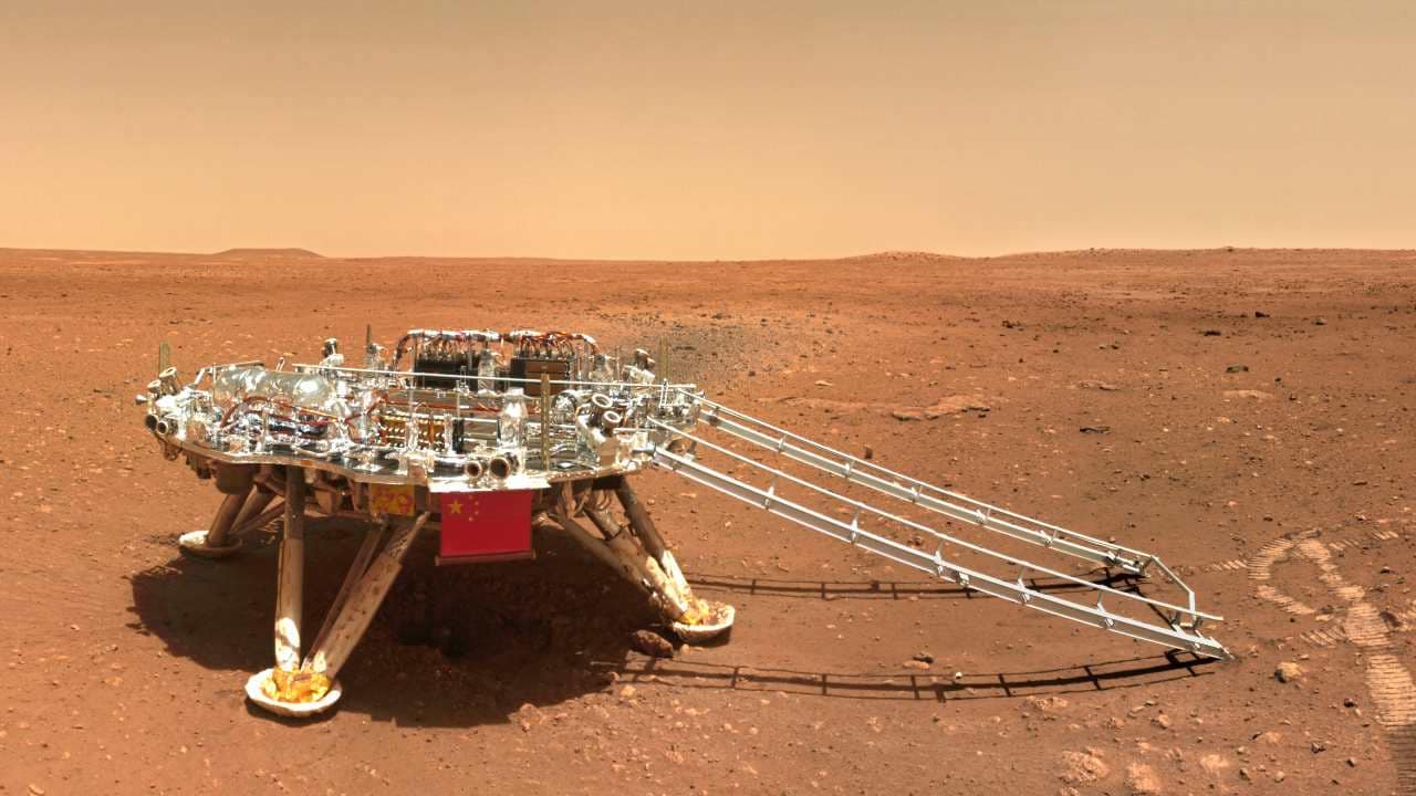 FOR USE WITH STORY CHINA MARS PHOTOS In this image released by the China National Space Administration (CNSA) on Friday, June 11, 2021, the landing platform with a Chinese national flag and outlines of the mascots for the 2022 Beijing Winter Olympics and Paralympics on Mars is seen from the rover Zhurong. China on Friday released a series of photos taken by its Zhurong rover on the surface of Mars, including one of the rover itself taken by a remote camera. (CNSA via AP)