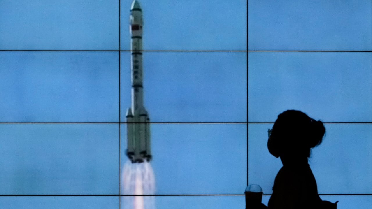 A woman wearing a face mask is silhouetted as she walks by a TV screen showing CCTV live telecast of the Long March-2F Y12 rocket carrying a crew of Chinese astronauts in a Shenzhou-12 spaceship lifts off at the Jiuquan Satellite Launch Center, at a shopping mall in Beijing. Image credit: AP Photo/Andy Wong