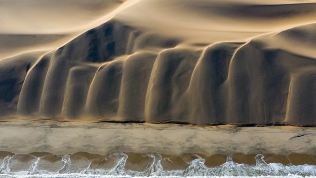 Meeting: This picture is the result of a dream come true: the meeting of the desert and the ocean. As the drone climbed higher, the photographer noticed a particular atmosphere, where the light highlighted the delicious shapes of these dunes flowing into the South Atlantic Ocean. Image Courtesy: David Rouge Meeting: This picture is the result of a dream come true: the meeting of the desert and the ocean. As the drone climbed higher, the photographer noticed a particular atmosphere, where the light highlighted the delicious shapes of these dunes flowing into the South Atlantic Ocean. Image Courtesy: David Rouge