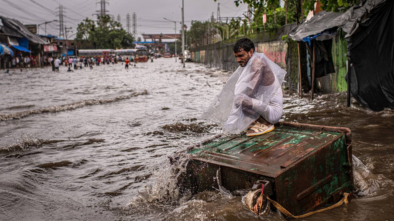 A resident sits on top of a dumpster surrounded by flood waters in the Scion neighborhood, along the Mithi River, of Mumbai, India, Aug. 4, 2019. By Bryan Denton c.2019 The New York Times
