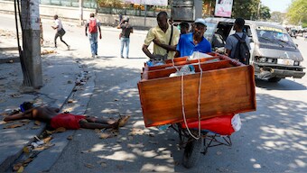 A man pushes a cart past the body of a man shot by unidentified assailants in downtown Port-au-Prince where gangs are thought to control 80 per cent of the territory. AP