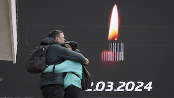 A couple embrace next to a screen with displayed mournful message in St. Petersburg, Russia, 24 March 2023. Russia observed a national day of mourning on Sunday after an attack on a suburban Moscow concert hall. AP