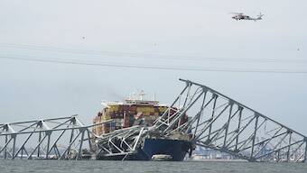 A Coast Guard helicopter passes a cargo ship that is stuck under the part of the structure of the Francis Scott Key Bridge after the ship his the bridge in Baltimore, US. AP
