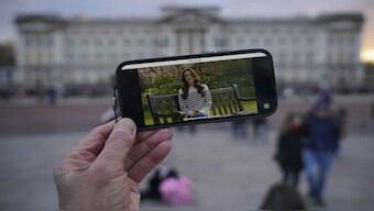 A person watches an announcement on a smart phone outside Buckingham Palace by Catherine, Princess of Wales. AP