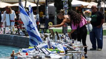 A woman holds a flower as people stand next to memorabilia and pictures of the hostages kidnapped in the deadly 7 October attack on Israel by the Palestinian Islamist group Hamas from Gaza, at Dizengoff Square in Tel Aviv, on 11 April, 2024. Reuters