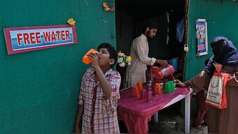 A young boy quenches his thirst as a volunteer distributes drinking water next to a bus stand on a hot summer day in Hyderabad, India, March 21, 2024 | Source: AP