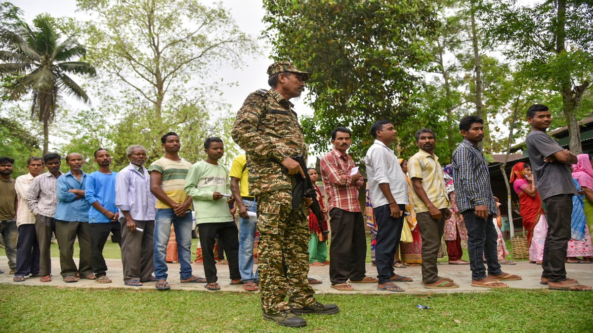 A security personnel stands guard as voters wait in a queue at a polling station to cast their votes for the first phase of Lok Sabha elections, in Nagaon district, 19 April 2024. PTI A security personnel stands guard as voters wait in a queue at a polling station to cast their votes for the first phase of Lok Sabha elections, in Nagaon district, 19 April 2024. PTI