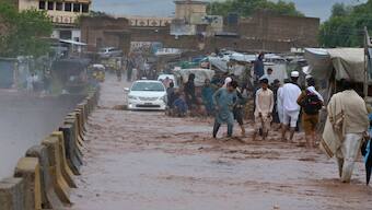 People wade through a flooded bridge on a stream, which is overflowing following heavy rains, on the outskirts of Peshawar, Pakistan, Monday, April 15, 2024. - AP