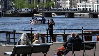 A woman takes a photograph as a boat cruises along a canal in Amsterdam, on April 12, 2024. AFP file