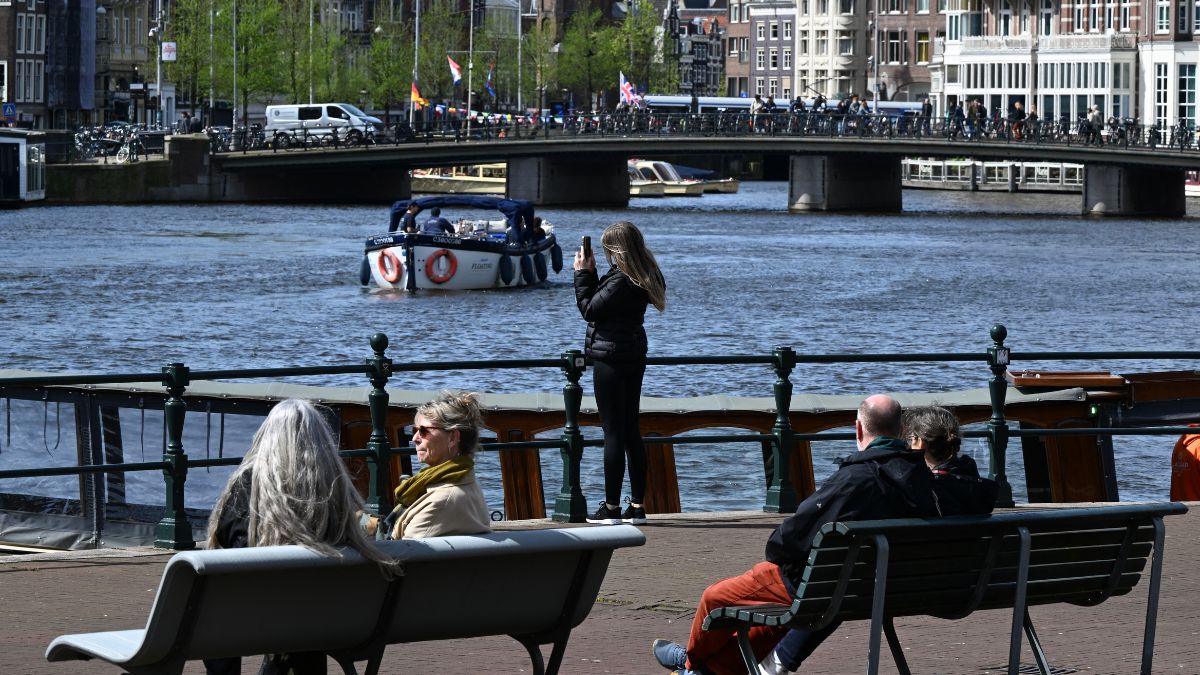 A woman takes a photograph as a boat cruises along a canal in Amsterdam, on April 12, 2024. AFP file A woman takes a photograph as a boat cruises along a canal in Amsterdam, on April 12, 2024. AFP file