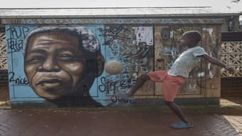 A child kicks a football in front of a mural of Nelson Mandela, in Soweto, South Africa. Source: AP