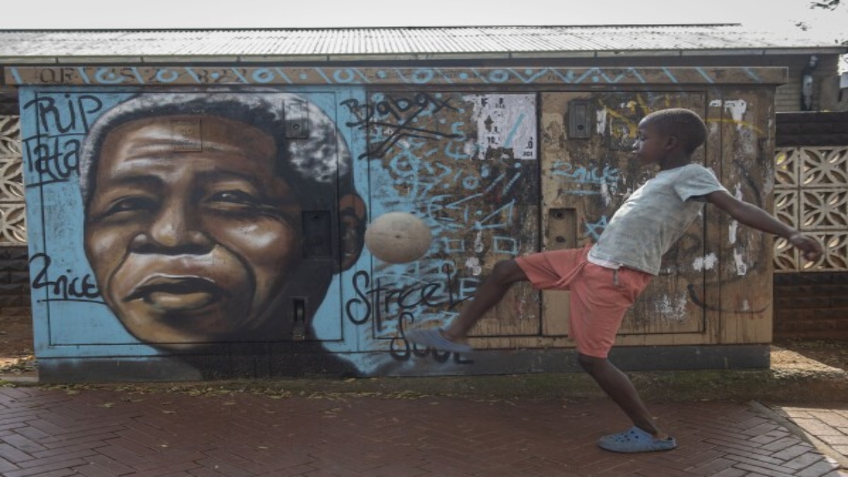 A child kicks a football in front of a mural of Nelson Mandela, in Soweto, South Africa. Source: AP A child kicks a football in front of a mural of Nelson Mandela, in Soweto, South Africa. Source: AP