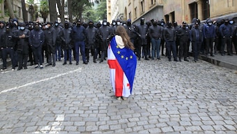 A demonstrator with draped Georgian national and EU flags stands in font of police blocking the way to the Parliament building, during an opposition protest against "the Russian law" in the centre of Tbilisi, Georgia. Georgia's parliament on Tuesday passed the foreign agents bill, evoking strong reactions from the people. AP
