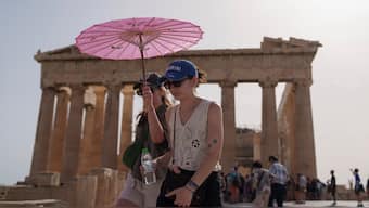 Tourists with an umbrella walk in front of the Parthenon at the ancient Acropolis in central Athens. AP