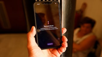 A man holds a mobile phone which displays an overheating warning due the high temperature in the street, that says, 'The temperature of the iPhone needs to cool down before you can use it' during a heatwave in Seville, southern Spain, in July 2022. Reuters
