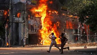 Men run past a shopping center which was set on fire by protesters during a rally against Prime Minister Sheikh Hasina and her government demanding justice for the victims killed in the recent countrywide deadly clashes, in Dhaka, Bangladesh, on Sunday. AP