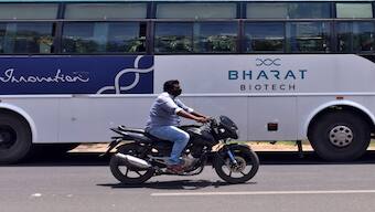 A man rides his motorbike past a parked bus of India's biotechnology company Bharat Biotech outside its office in Hyderabad, India. Image courtesy: Reuters