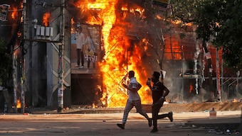 Men run past a shopping center which was set on fire by protesters during a rally against Prime Minister Sheikh Hasina and her government in Dhaka, Bangladesh, Sunday, Aug. 4, 2024. (AP Photo/Rajib Dhar)