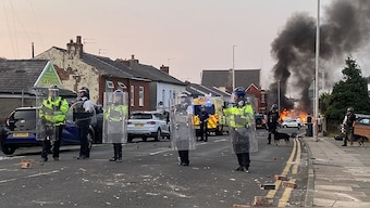 Smoke billows from a fire started by protesters as riot police stand guard after disturbances near the Southport Islamic Society Mosque in Southport, northwest England. AFP