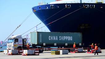 A truck transports a container next to a cargo vessel at a port in Qingdao, Shandong province, China. Source: REUTERS / FILE. 