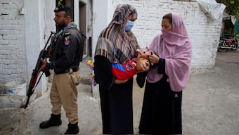 A police officer stands guard as a health worker, right, administers a polio vaccine to a child in a neighbourhood of Peshawar, Pakistan on Sept. 9, 2024. AP