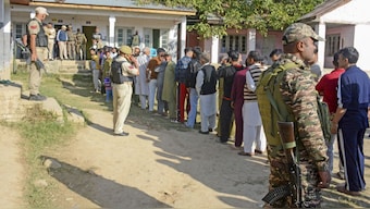 Security personnel stand guard as voters wait in a queue to cast their votes at a polling booth during the third and final phase of Jammu and Kashmir Assembly elections, at Pattan in Baramulla district on October 1. File image/PTI