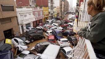 A woman looks out from her balcony as vehicles are trapped in the street during flooding in Valencia. AP
