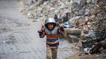 A displaced boy covers his head with a pan as he runs from the rain past building rubble at the Bureij refugee camp in the central Gaza Strip on November 24, 2024, amid the ongoing war between Israel and the Palestinian Hamas militant group. Image- AFP

