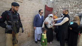 A police officer stands guard as a health worker administers a polio vaccine to a child, in Peshawar, Pakistan. AP