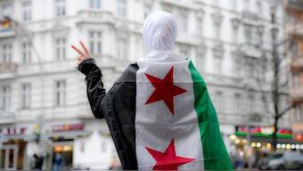 A Syrian girl flashes victory sign in a street in Berlin while wearing a Syrian opposition flag, December 10, 2024. File Image/AP