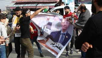 Syrian refugees hold a banner bearing a picture of President Bashar al-Assad with Arabic writing referring to him as a "pig" in the eastern Lebanese town of Majdel Anjar in the Bekaa Valley on December 8, 2024, following the fall of the Syrian capital to anti-government fighters. AFP