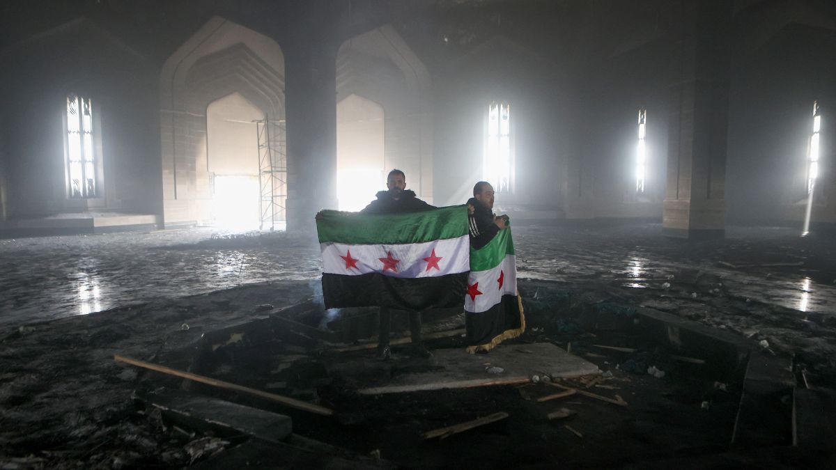 TOPSHOT - Rebel fighters stand with the flag of the revolution on the burnt gravesite of Syria's late president Hafez al-Assad at his mausoleum in the family's ancestral village of Qardaha in the western Latakia province on December 11, 2024. AFP TOPSHOT - Rebel fighters stand with the flag of the revolution on the burnt gravesite of Syria's late president Hafez al-Assad at his mausoleum in the family's ancestral village of Qardaha in the western Latakia province on December 11, 2024. AFP