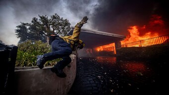 A firefighter jumps over a fence while fighting the Palisades Fire in the Pacific Palisades neighborhood of Los Angeles, Tuesday, January 7, 2025. AP