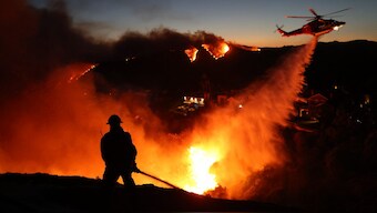 Fire personnel respond to homes destroyed while a helicopter drops water as the Palisades Fire grows in Pacific Palisades, California. AFP