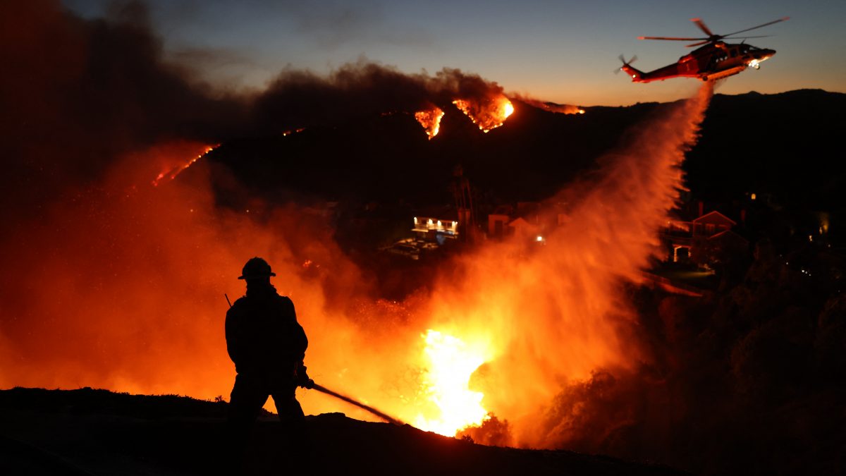 Fire personnel respond to homes destroyed while a helicopter drops water as the Palisades Fire grows in Pacific Palisades, California. AFP Fire personnel respond to homes destroyed while a helicopter drops water as the Palisades Fire grows in Pacific Palisades, California. AFP