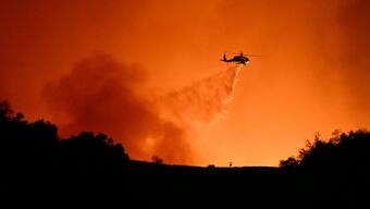 A helicopter drops water on smoke and flames from the Palisades Fire burning behind Mulholland drive towards the Encino neighborhood in Los Angeles, California, January 10, 2025.  Image- AFP