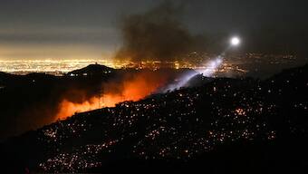 The light of a fire fighting helicopter illuminates a smouldering hillside as the Palisades fire grows near the Mandeville Canyon neighborhood and Encino, California, on January 11, 2025.- Image- AFP