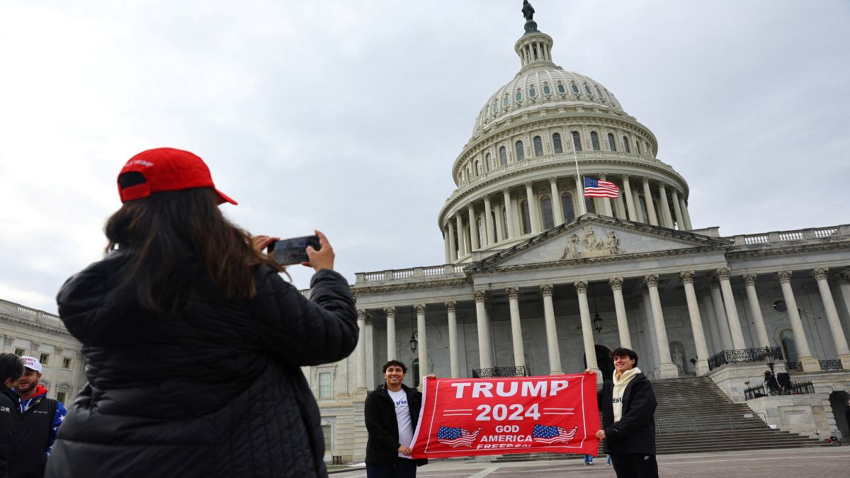 A woman clicks a picture as people hold a placard in favour of US President-elect Donald Trump in front of the US Capitol building ahead of the presidential inauguration in Washington, on, January 18. The oath ceremony has now been moved indoors because of the freezing temperatures in the capital city. Reuters A woman clicks a picture as people hold a placard in favour of US President-elect Donald Trump in front of the US Capitol building ahead of the presidential inauguration in Washington, on, January 18. The oath ceremony has now been moved indoors because of the freezing temperatures in the capital city. Reuters