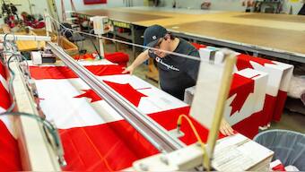A worker adjusts a Canadian flag before cutting it to size at Flags Unlimited in Barrie, Ontario, Canada, February 12, 2025. File Image/Reuters