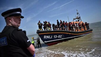 A British police officer stands guard on the beach of Dungeness, on the southeast coast of England, on 15 June, 2022, as Royal National Lifeboat Institution's (RNLI) members of staff help migrants to disembark. (Photo: AFP)