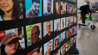 A man rides past a banner with pictures of hostages, on the day the bodies of deceased Israeli hostages are handed over under the terms of a ceasefire. Reuters
