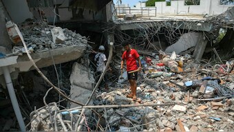 People stand next to a destroyed building as rescuers look through the rubble to find survivors in Mandalay on March 29, 2025, a day after an earthquake struck central Myanmar. AFP