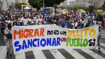 People hold a banner that reads in Spanish, "Migrating is not a crime; sanctioning a people is," at a government-organized march to protest the deportation from the U.S. of alleged members of the Venezuelan Tren de Aragua gang, who were transferred to an El Salvador prison, in Caracas, Venezuela. AP